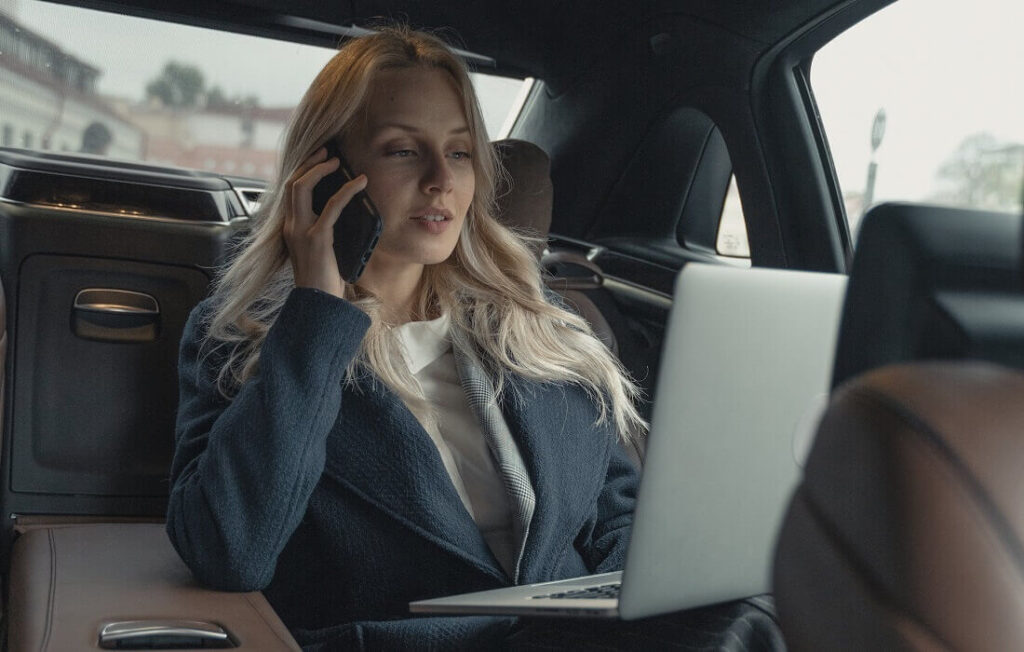 Woman working on phone and laptop in backseat of a car