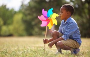 boy with pinwheel squats in field of grass