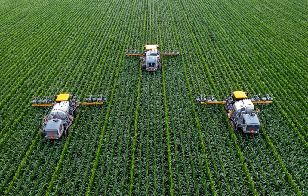 three large tractors harvesting crops in green field
