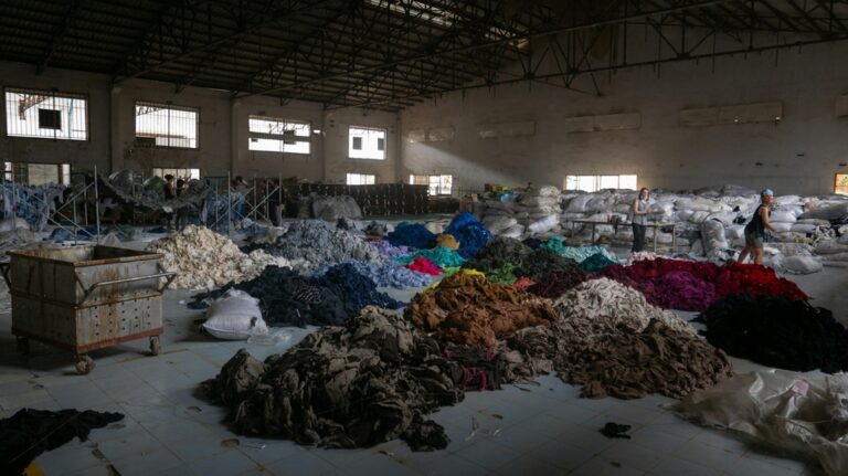 piles of clothes sorted into colored piles sit in dim warehouse