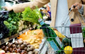 woman with shopping basket picks up leafy vegetable
