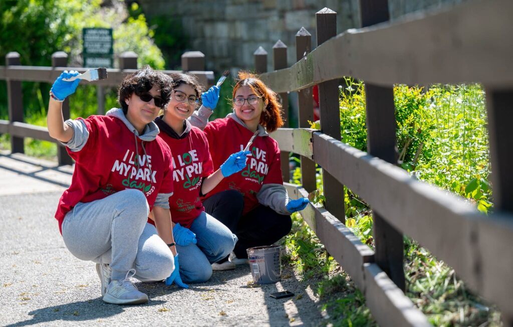 three people with paintbrushes pose while working on fence