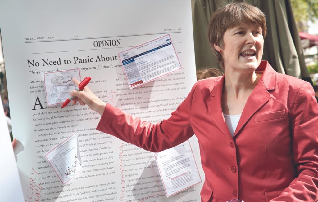 woman in red blazer gestures at report during presentation