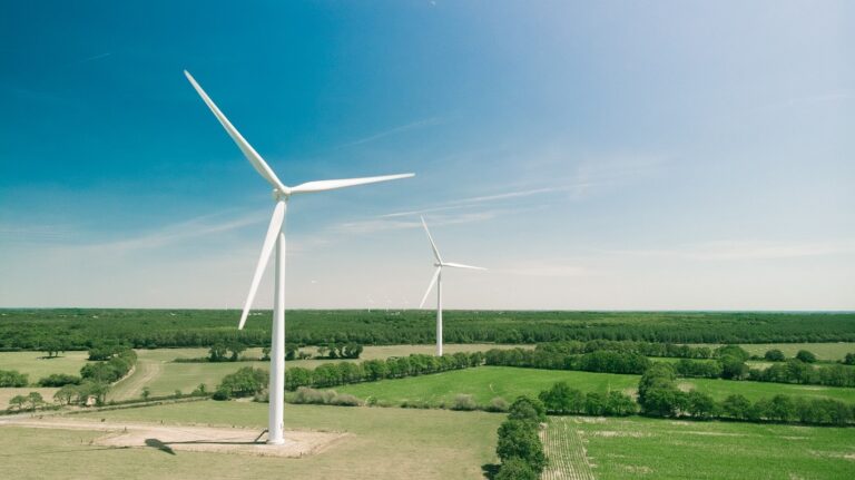 white wind turbines against backdrop of green farmlands