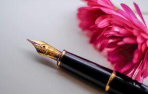 pluma estilográfica negra y dorada junto a una flor rosa